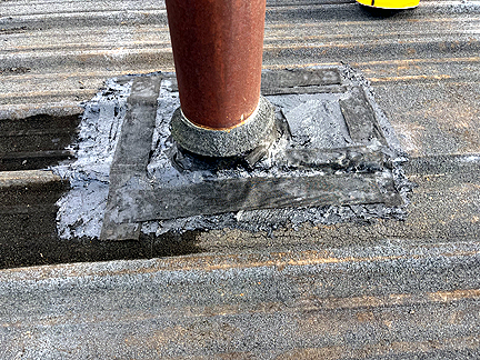 Pipe penetration in BUR Rolled Asphalt Modified Roof, has four voids at the base, with water pooled in the interior.